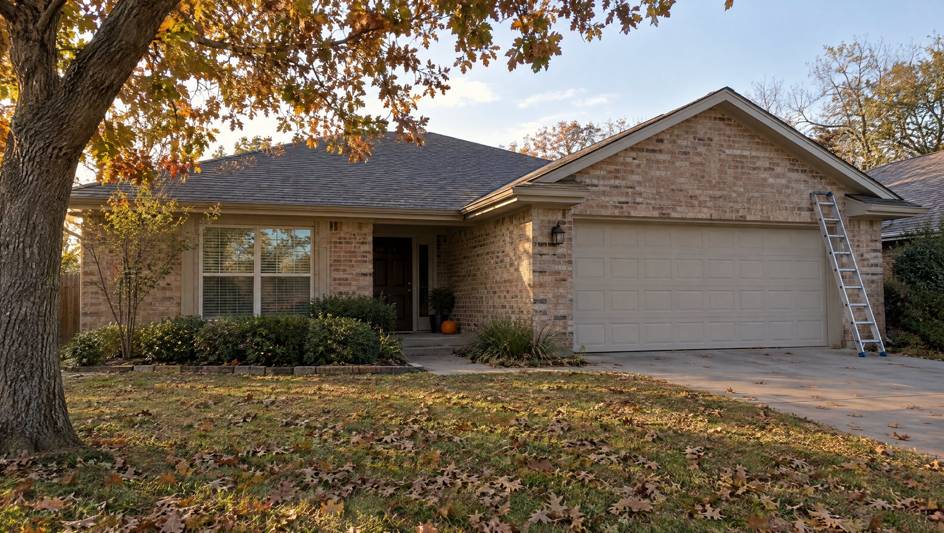 One-story brick home in late October with a pumpkin on the steps and a ladder against the garage