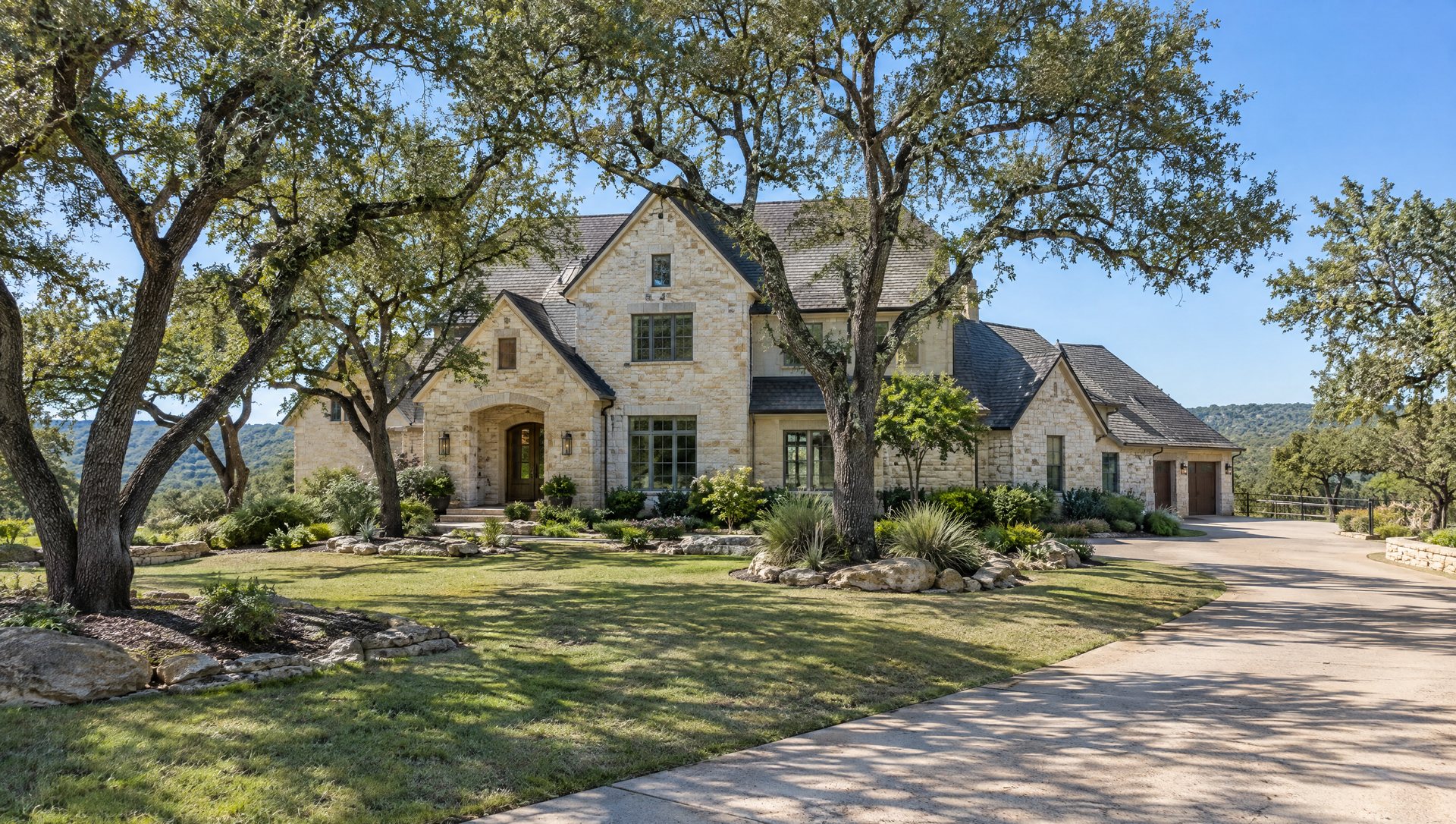 Large two-story limestone home with a steep multi-gable roof and several mature live oaks.