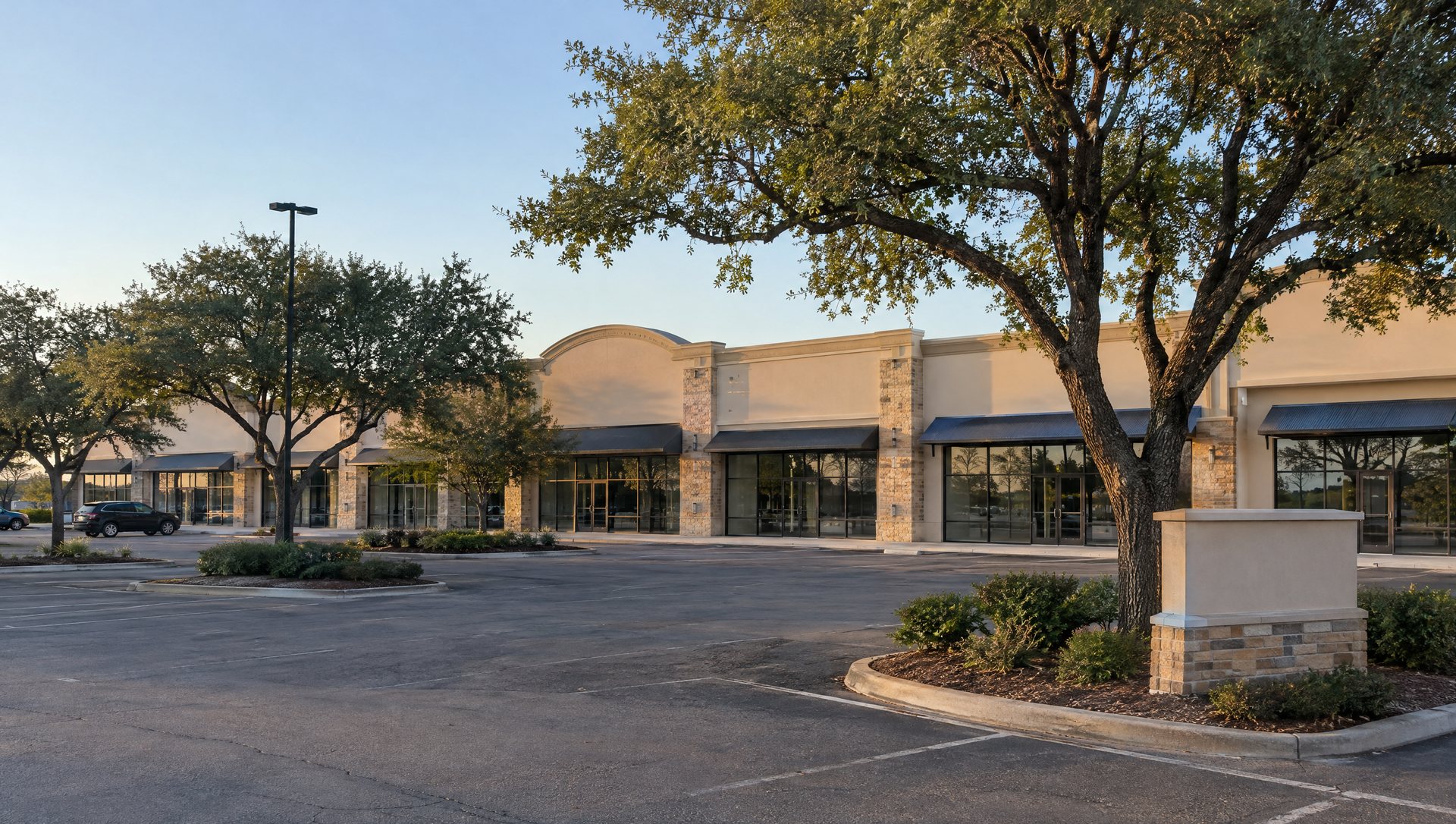 A small shopping center with a shared parapet, parking-island oaks and a monument sign base before any lights go up.