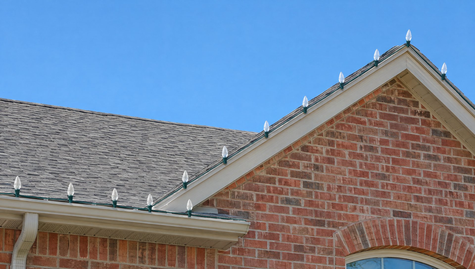 Unlit C9 bulbs in a straight, even line along a gutter and gable on a brick home in daylight.