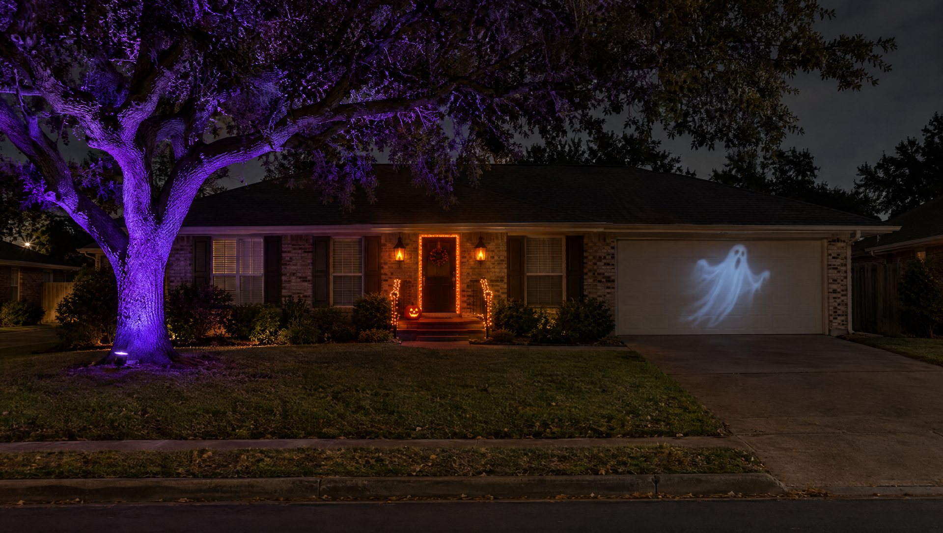 Austin brick ranch house lit for Halloween with an orange door, purple-uplit oak and a ghost projection on the garage