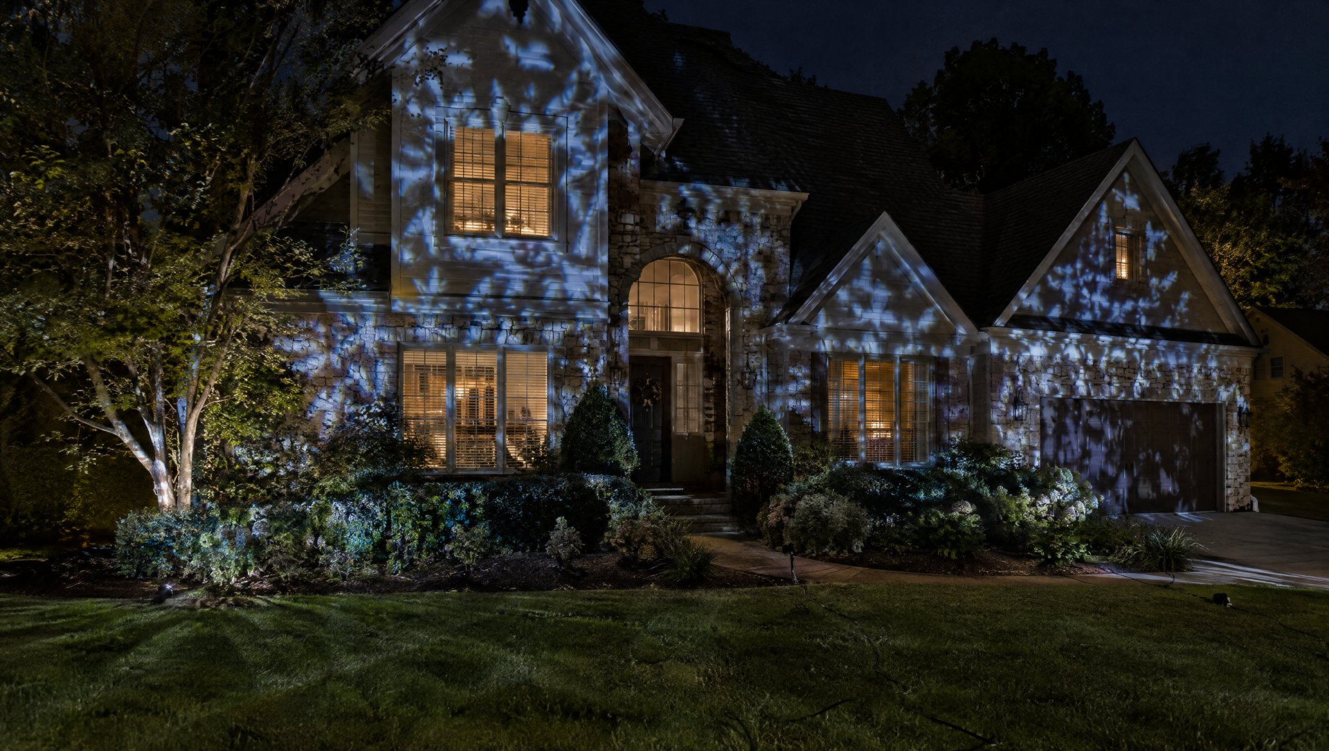 Halloween projector pattern scattered across windows and shrubs on a busy facade