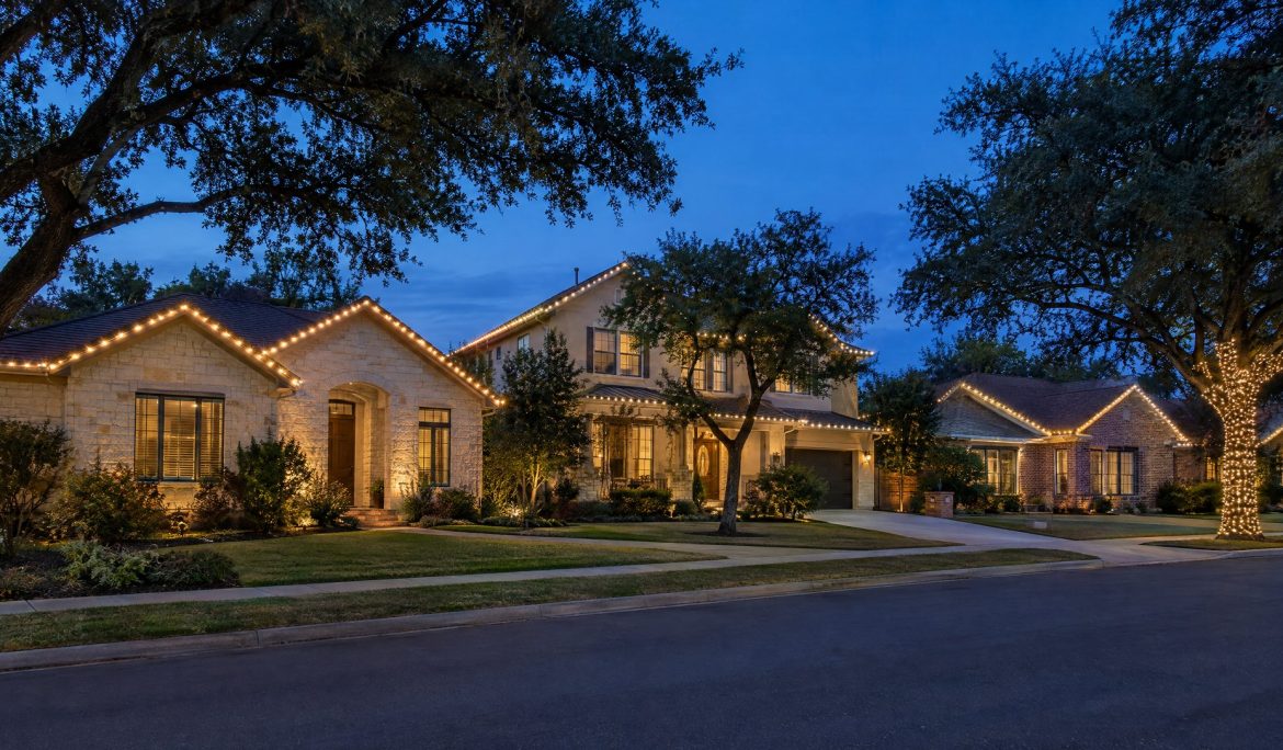 Austin street at blue hour with several homes outlined in straight warm white roofline lights.