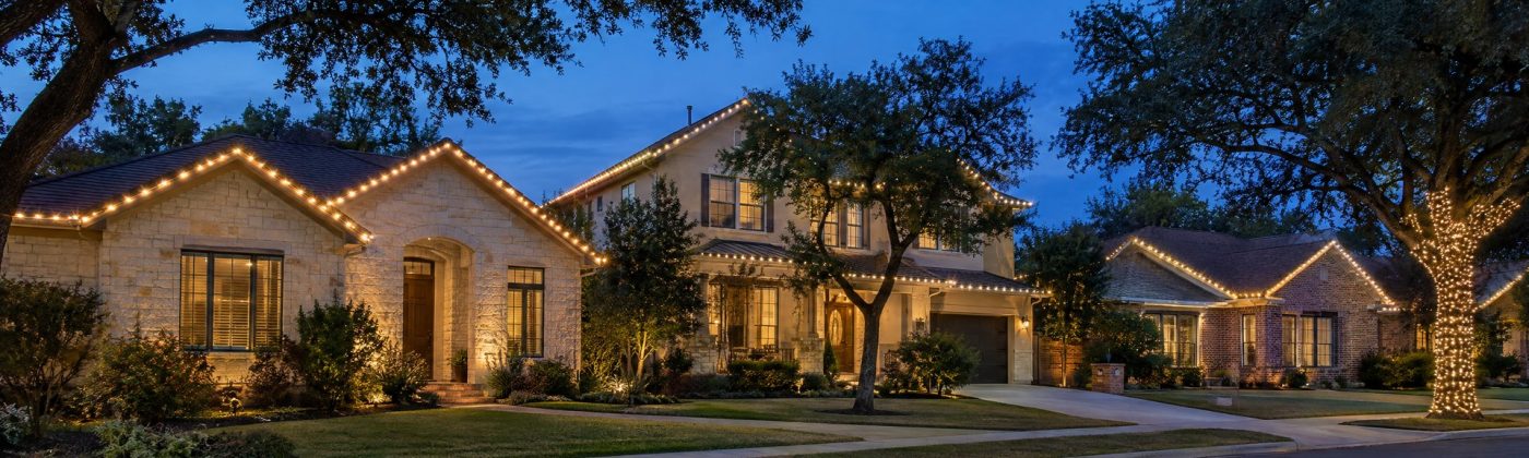 Austin street at blue hour with several homes outlined in straight warm white roofline lights.