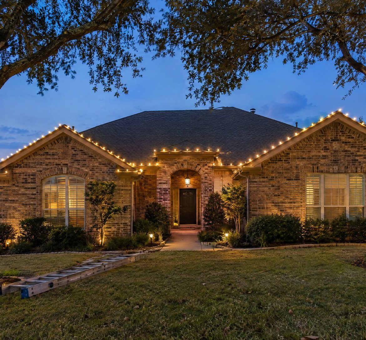 Home at dusk with freshly hung warm white roofline lights and wrapped tree trunks