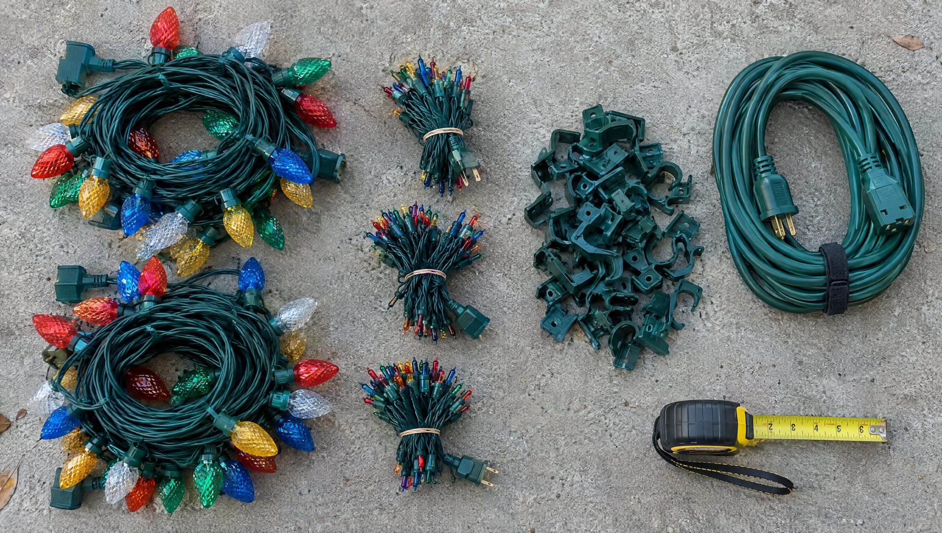 Christmas light hanging supplies laid out on a driveway: C9 strings, mini lights, clips, cord and tape measure