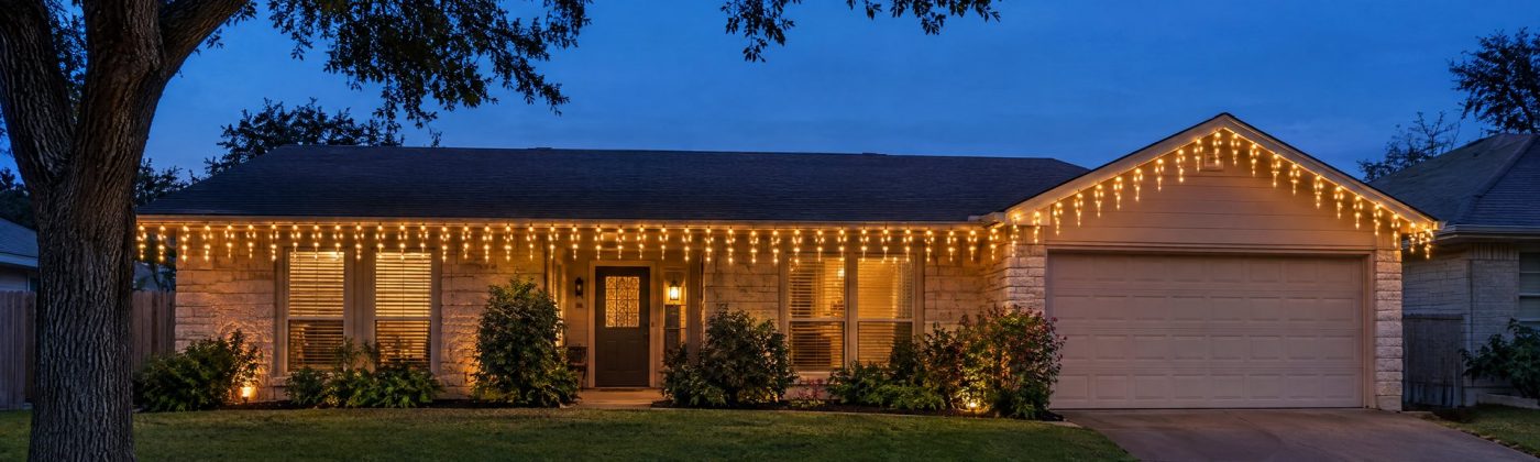 Evenly hanging warm white icicle lights along a ranch home's eave at night