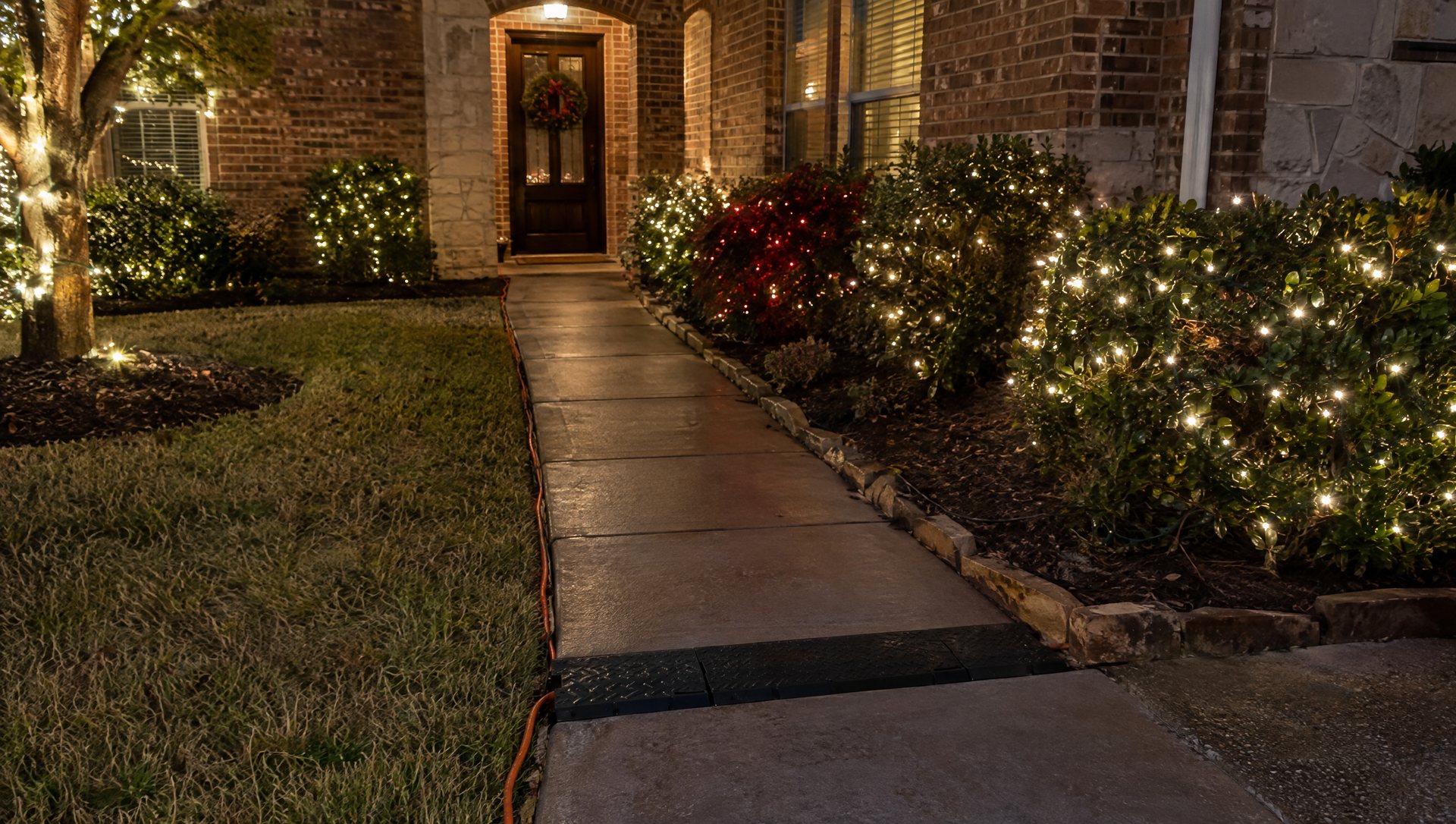 Front walkway at night with a light cord routed along the lawn edge and a ramp cover at the crossing