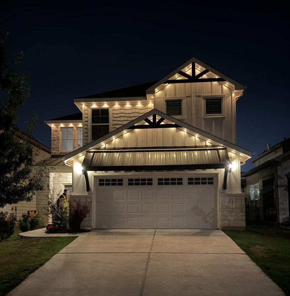 Two-story home with warm white roofline lights outlining the gables and garage roof