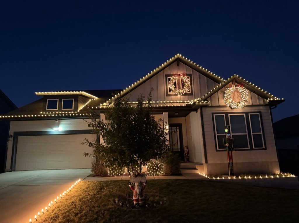 Farmhouse-style home with a warm white roofline, wreaths and walkway lights