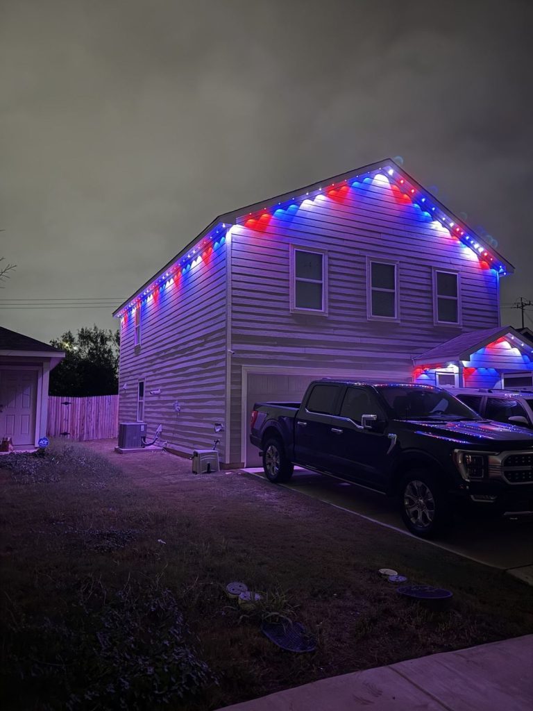 Two-story home in red, white and blue permanent lights, side view