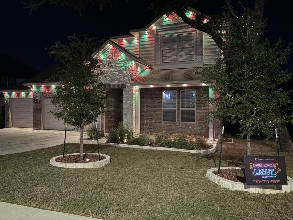 Two-story home with red and green permanent lights and landscaped beds