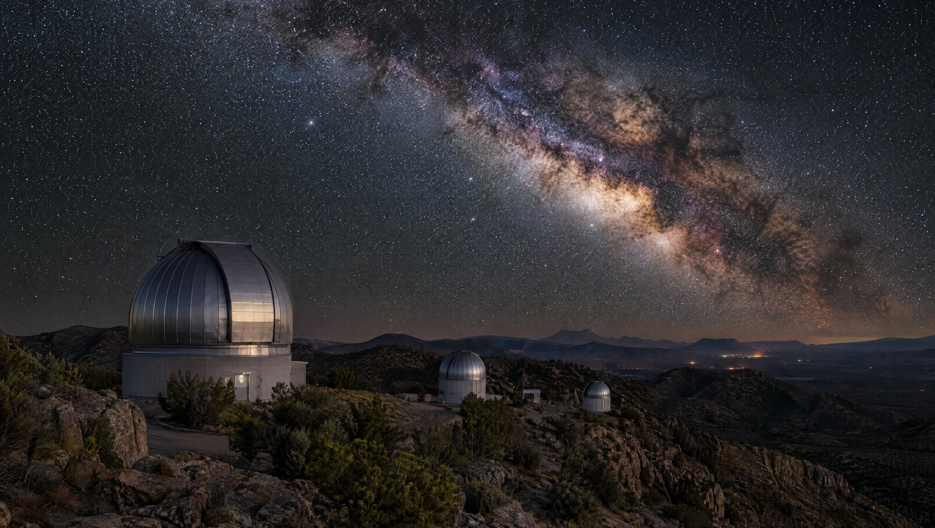 Observatory domes on a West Texas mountaintop under the Milky Way with dark desert hills below