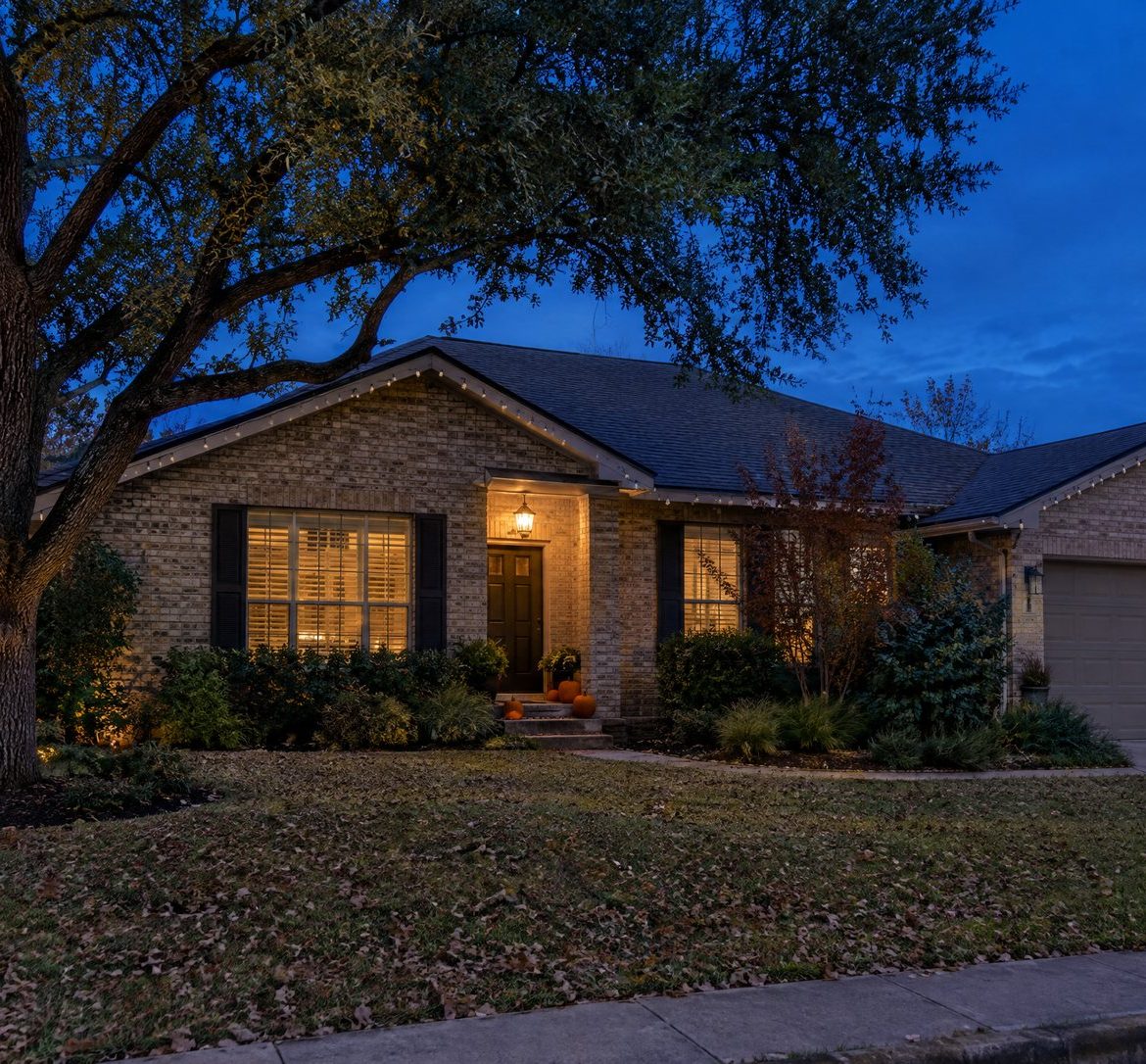 Is It Too Early to Put Up Christmas Lights in October? Install Now, Turn On Later Austin brick home at blue hour with unlit Christmas bulbs along the roofline and pumpkins on the steps