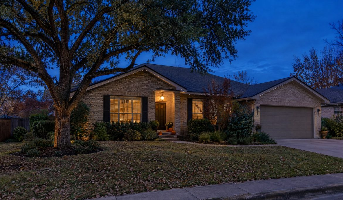 Austin brick home at blue hour with unlit Christmas bulbs along the roofline and pumpkins on the steps